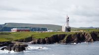 a rocket stands upright on a launch pad on a rocky outcrop beside the sea