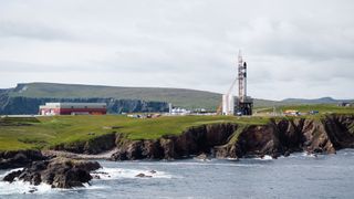 a rocket stands upright on a launch pad on a rocky outcrop beside the sea
