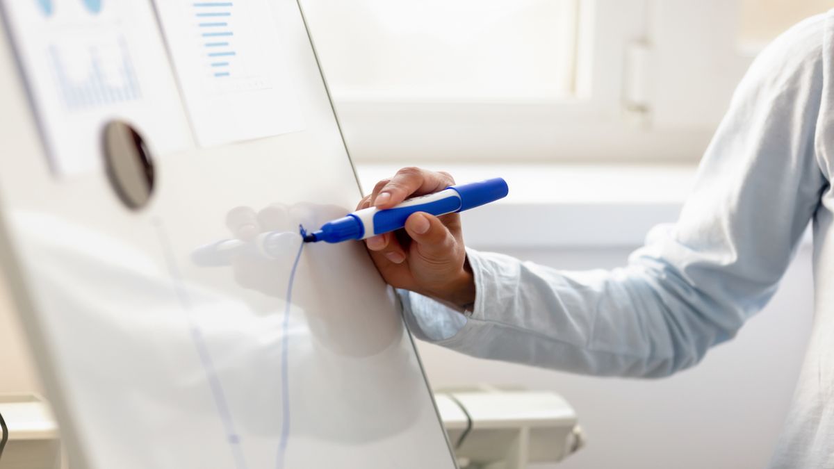 A woman draws a graph with an upward trend on a whiteboard.