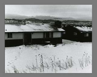 Black and white photograph of a house with snow on the grass at the front