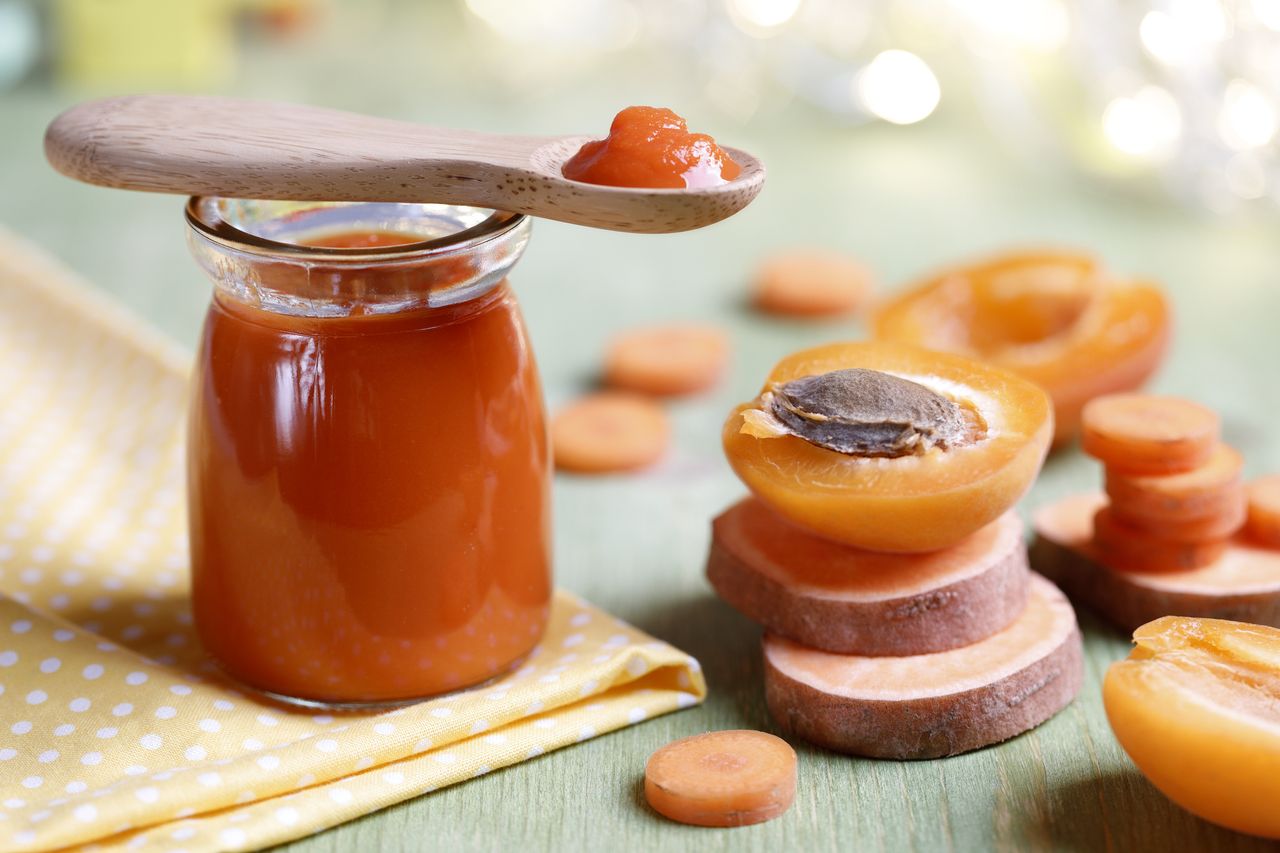 Apricot purée baby food in a jar next to some apricots