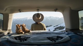 A hiker looks at the snowy mountains from the back of her car