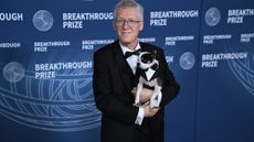 A man with gray hair wearing a black and white tuxedo holds a small black and white dog.