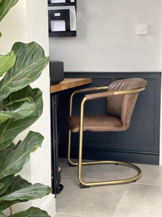 an office tucked into corner of home, with a wooden desk tucked against a blue and beige wall, and a plant to the left