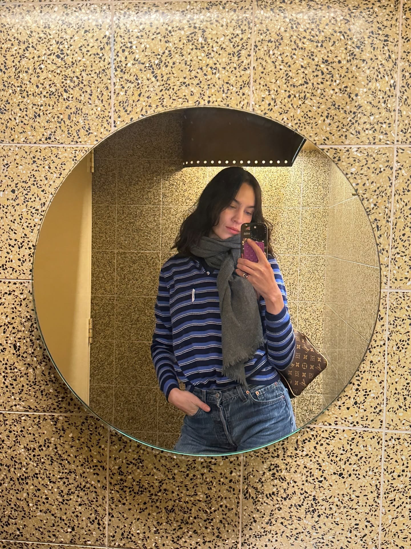 Alexa Chung takes a mirror selfie wearing a striped knit with a grey scarf and jeans.