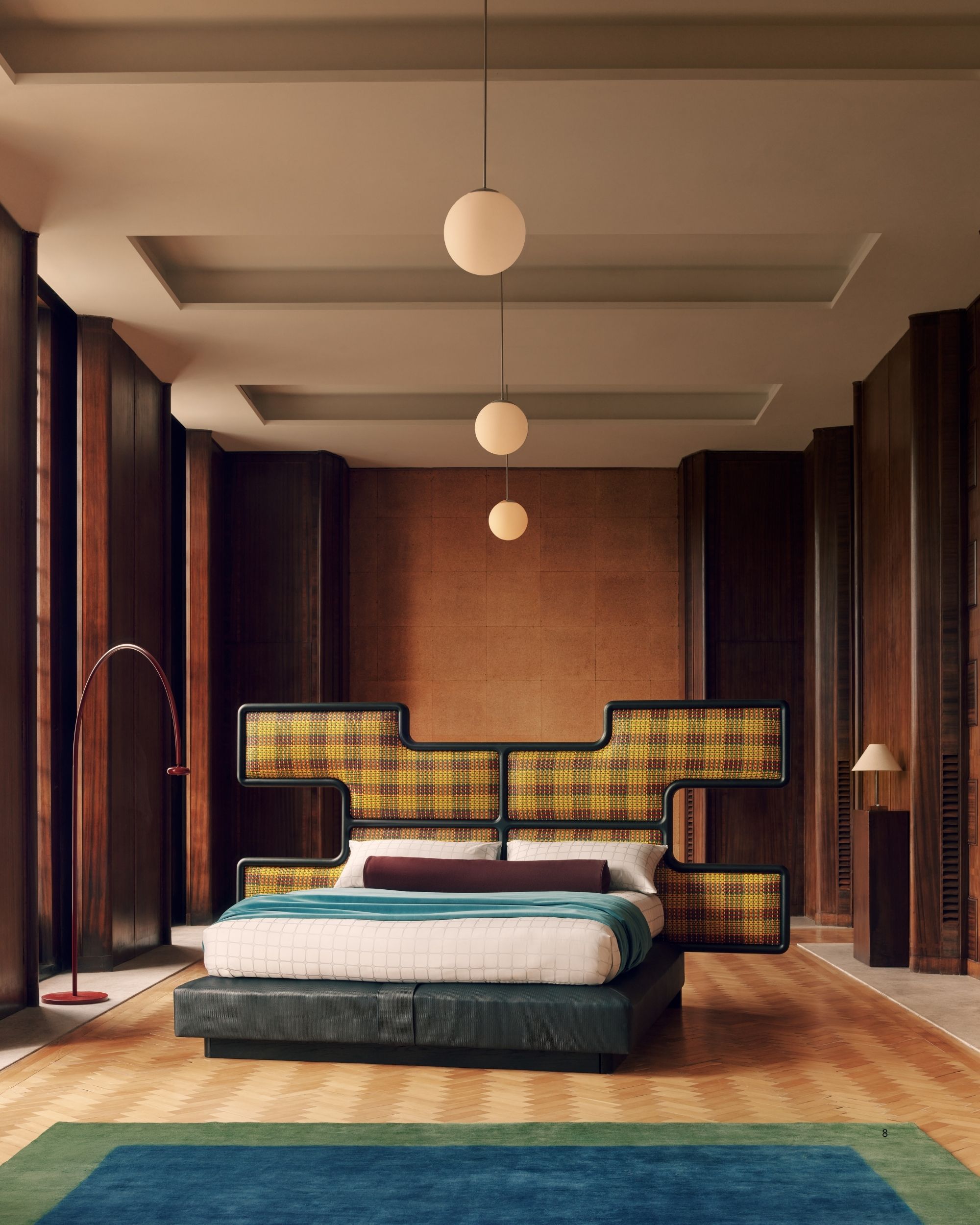 Image of a grand room with a giant bed in the middle that has a yellow plaid headboard in the shape of an X. 