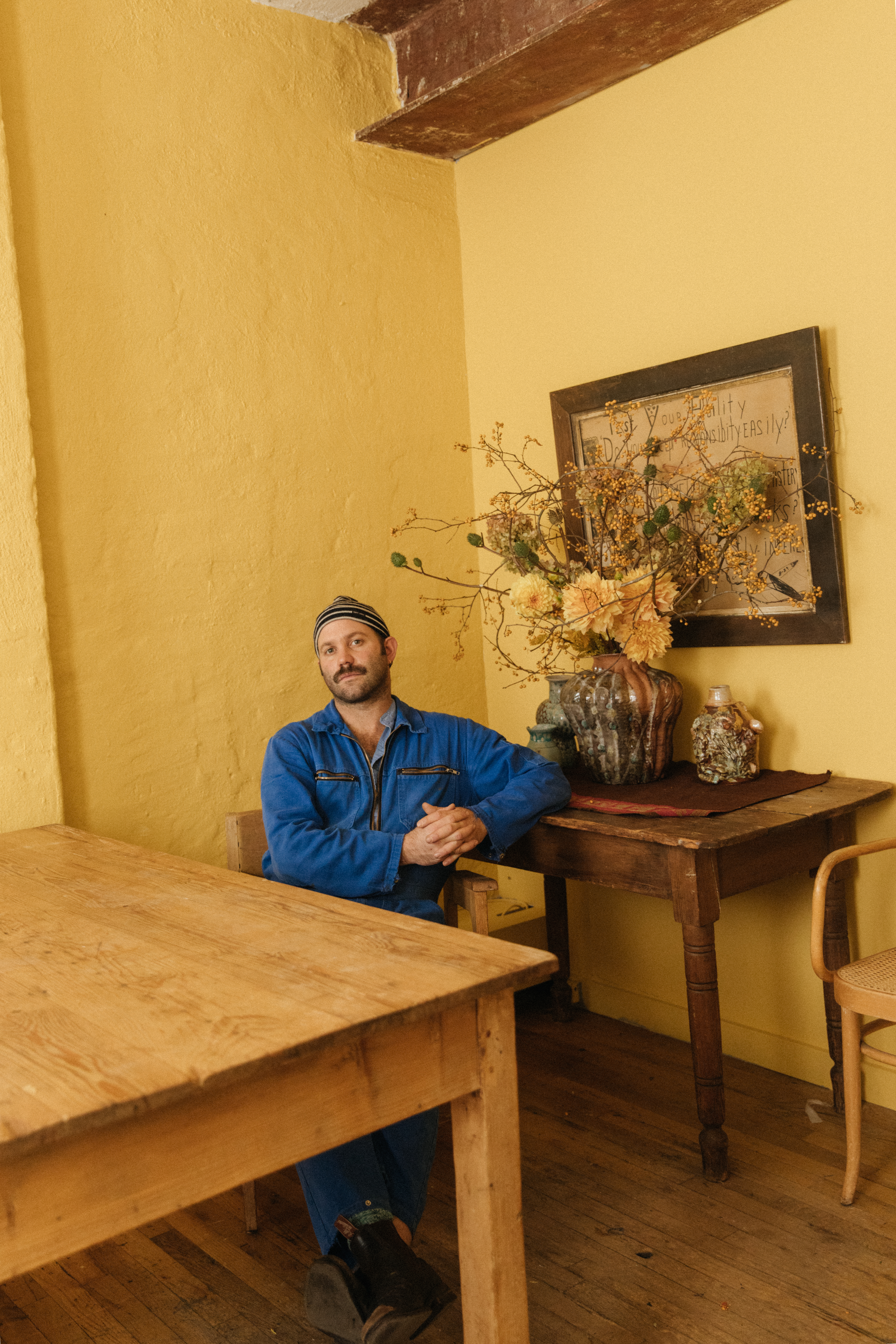 Curator Alex Tieghi-Walker sits at a table in a yellow room