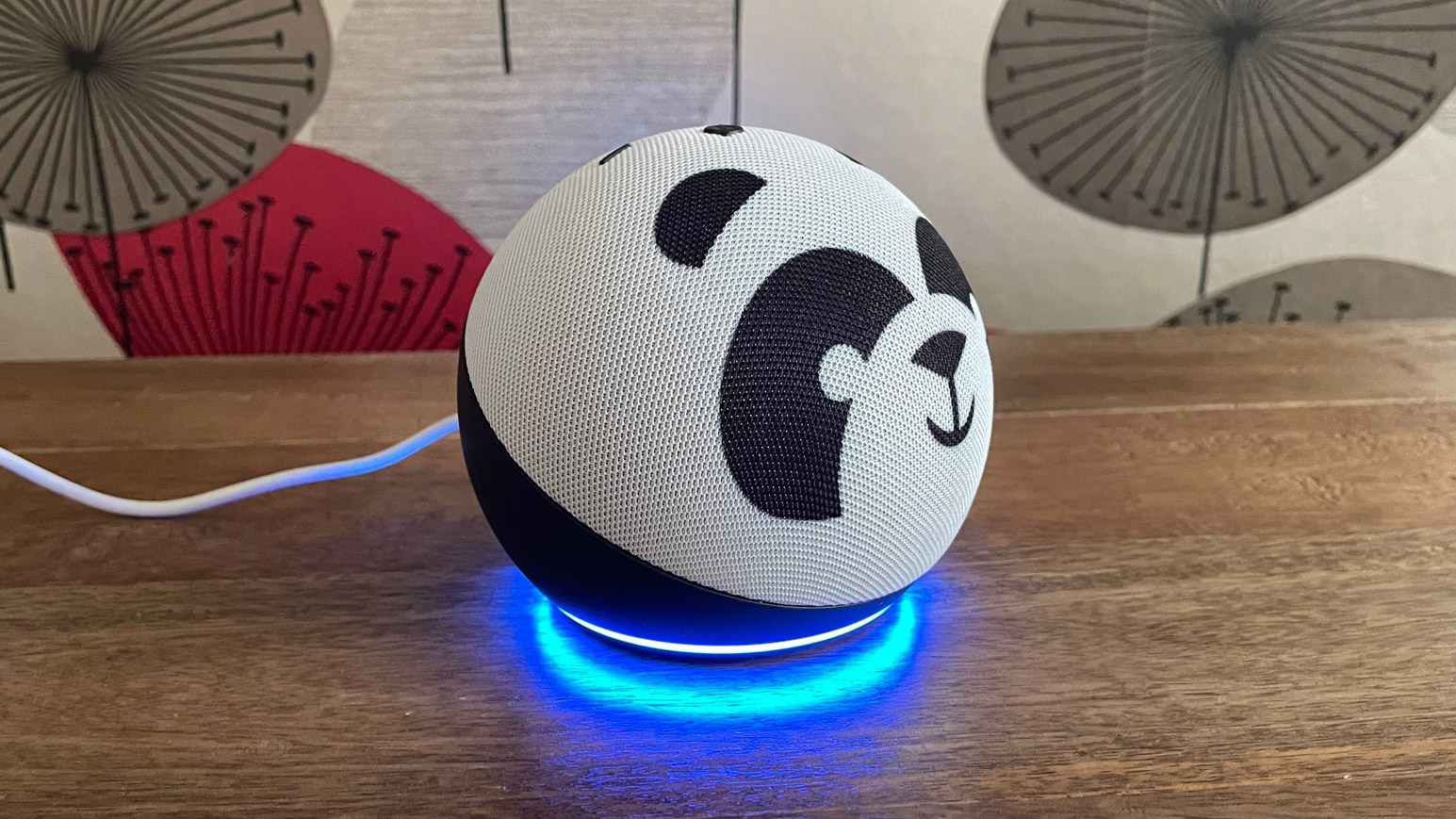 The side view of the Amazon Echo Dot Kids smart speaker on a wooden table with a patterned wall behind