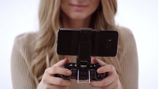 A woman holds an xbox wireless controller with a phone clip for mobile gaming