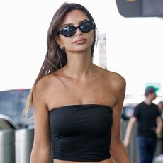 Emily Ratajkowski wears black sunglasse and a black tube top at the airport.