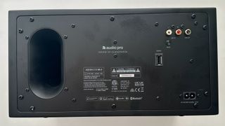 The rear panel of the Audio Pro Addon C10 MkII wireless speaker, featuring USB input and analogue audio inputs. On the right, there is. a large oval hole, which is a bass port