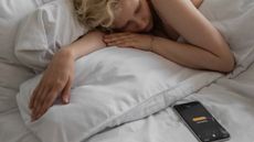 Woman sleeping in a bed with her iPhone alarm going off