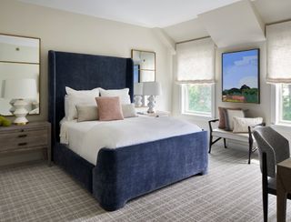 neutral bedroom with blue bed with oversized headboard and patterned carpet