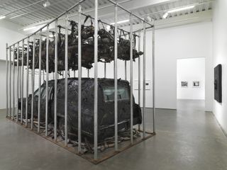 Installation view of Nari Ward, Peace Keeper, 1995. A hearse, mufflers and feathers in a steel cage.