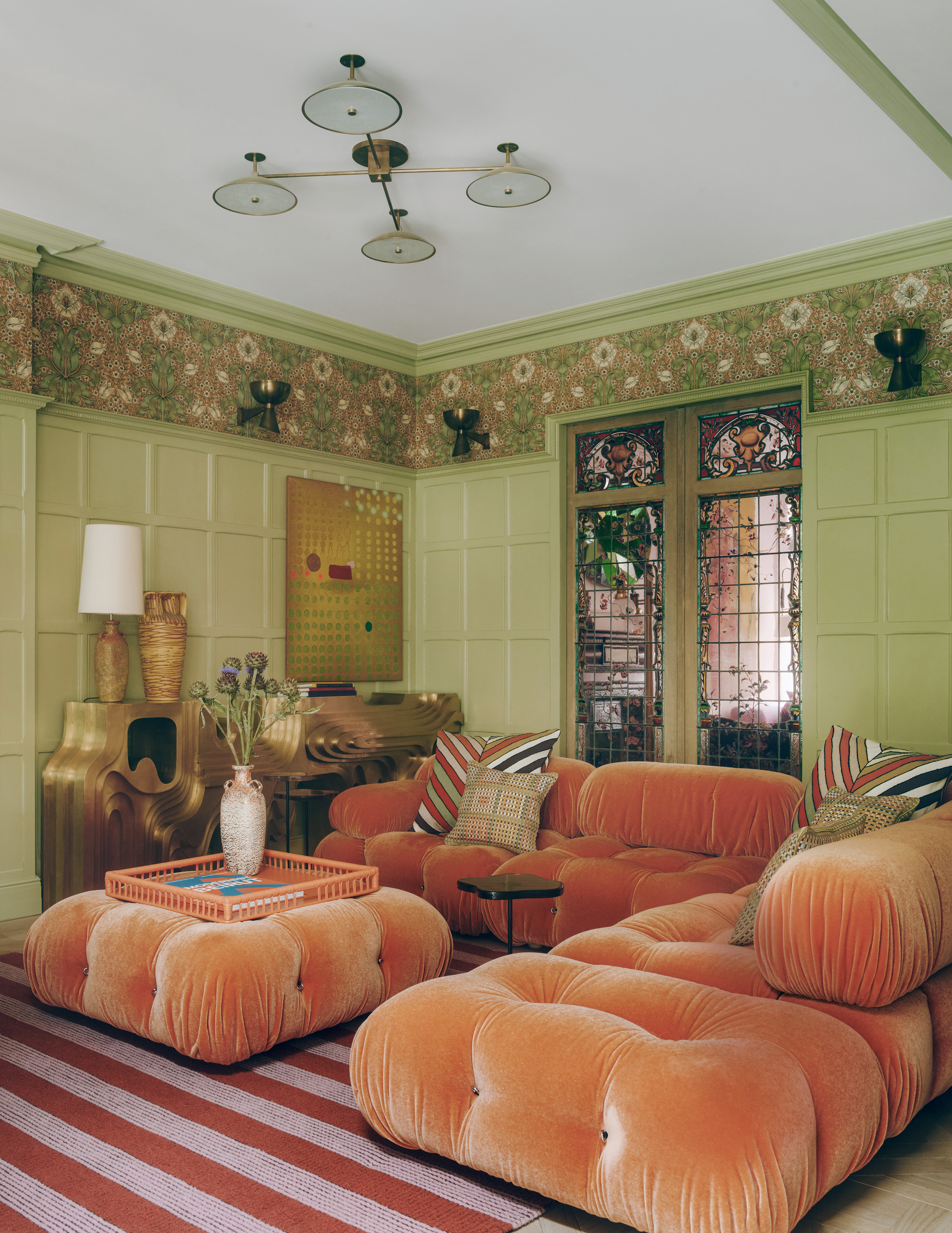 Lime green living room with paneled walls, orange sofa and pink and red striped rug