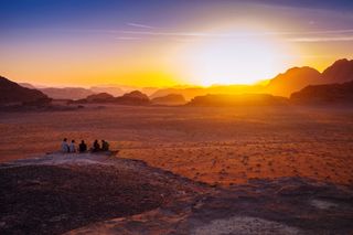 Rear View Of Friends Sitting On Rock At Wadi Rum During Sunset - stock photo