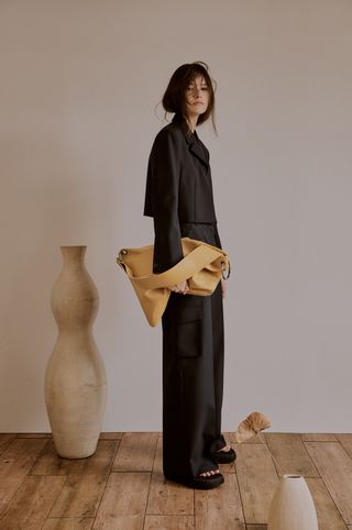 Woman stands holding a beige leather pouch