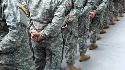 The backs of uniformed military soldiers standing in a line.
