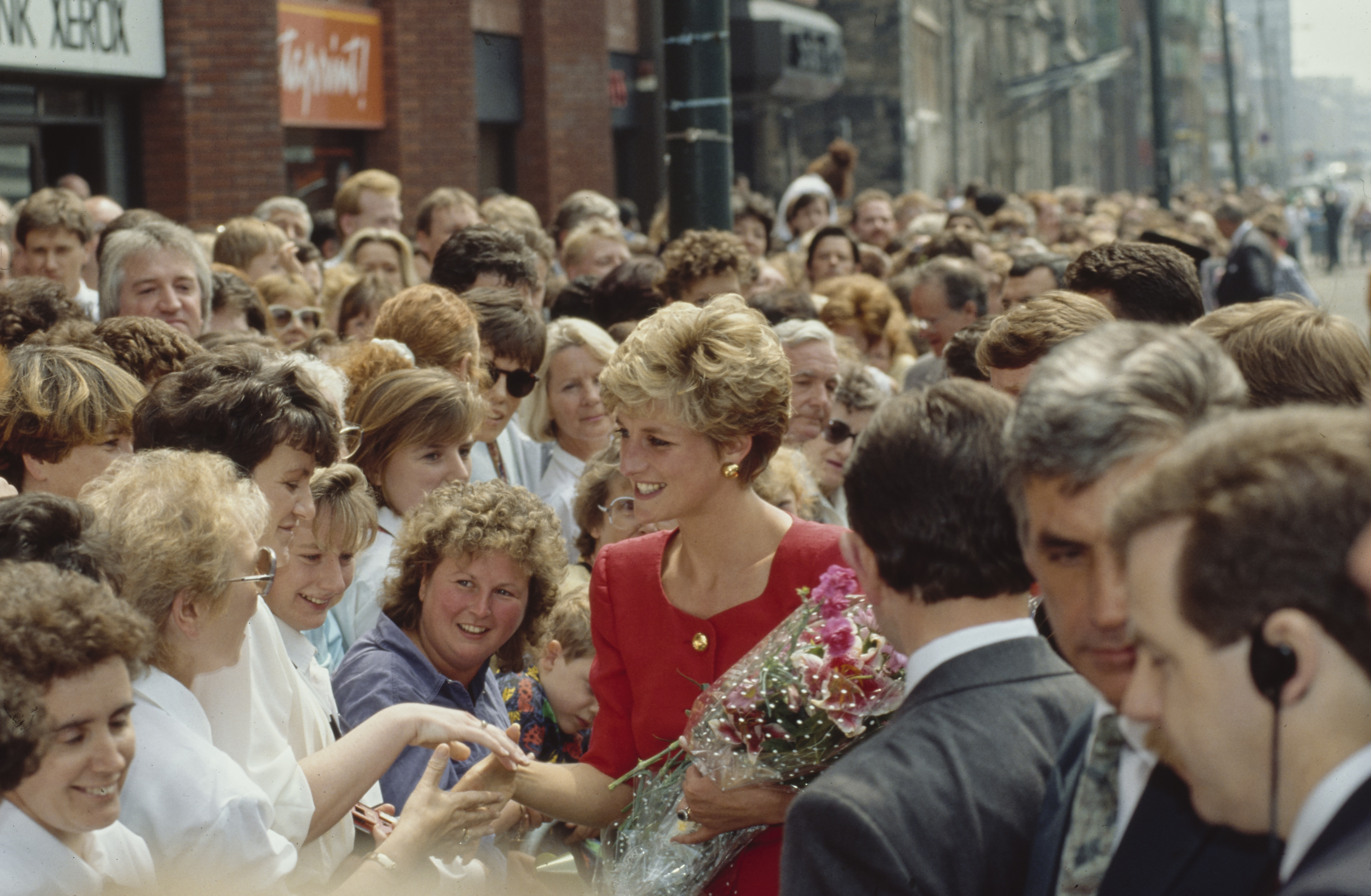 Princess Diana in a red dress shaking hands with fans in Belfast