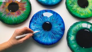 A shot of an artist's hand with an array of acrylic eye paintings