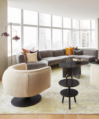 A living room with a large gray sectional, tall windows and a vintage boucle armchair