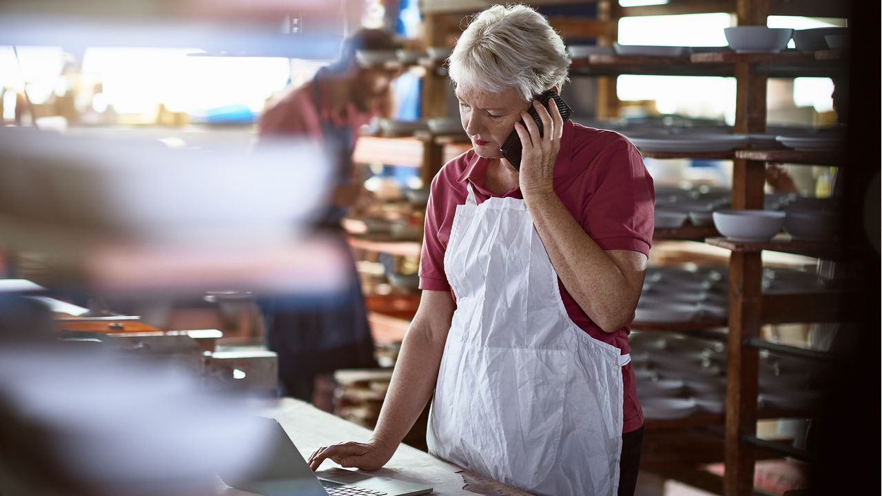 A restaurant owner talks on the phone while checking her laptop.