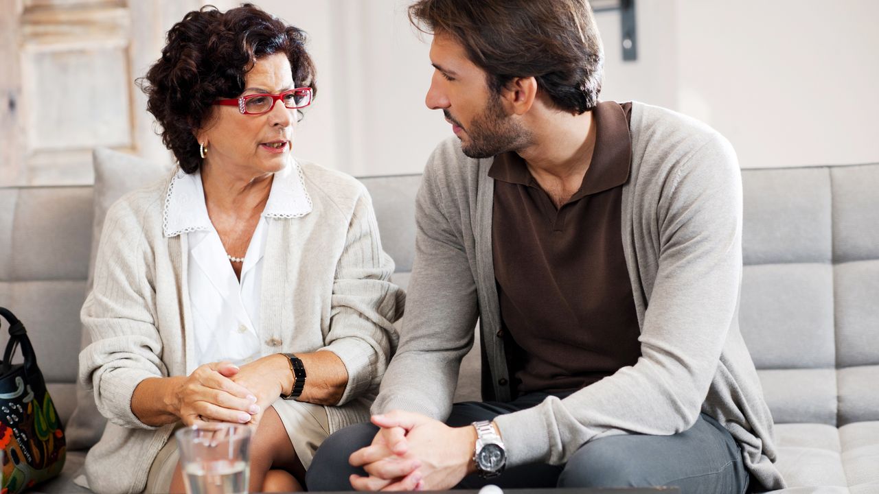 A mother and son have a serious talk while sitting next to each other on the sofa.