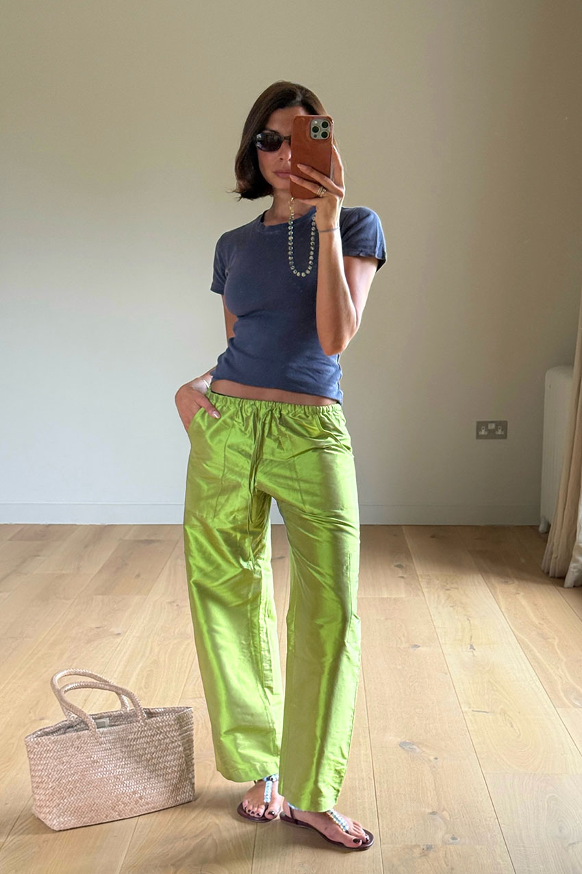 a woman wearing a blue baby tee, green pants, embellished t-strap flat sandals, and a woven bag