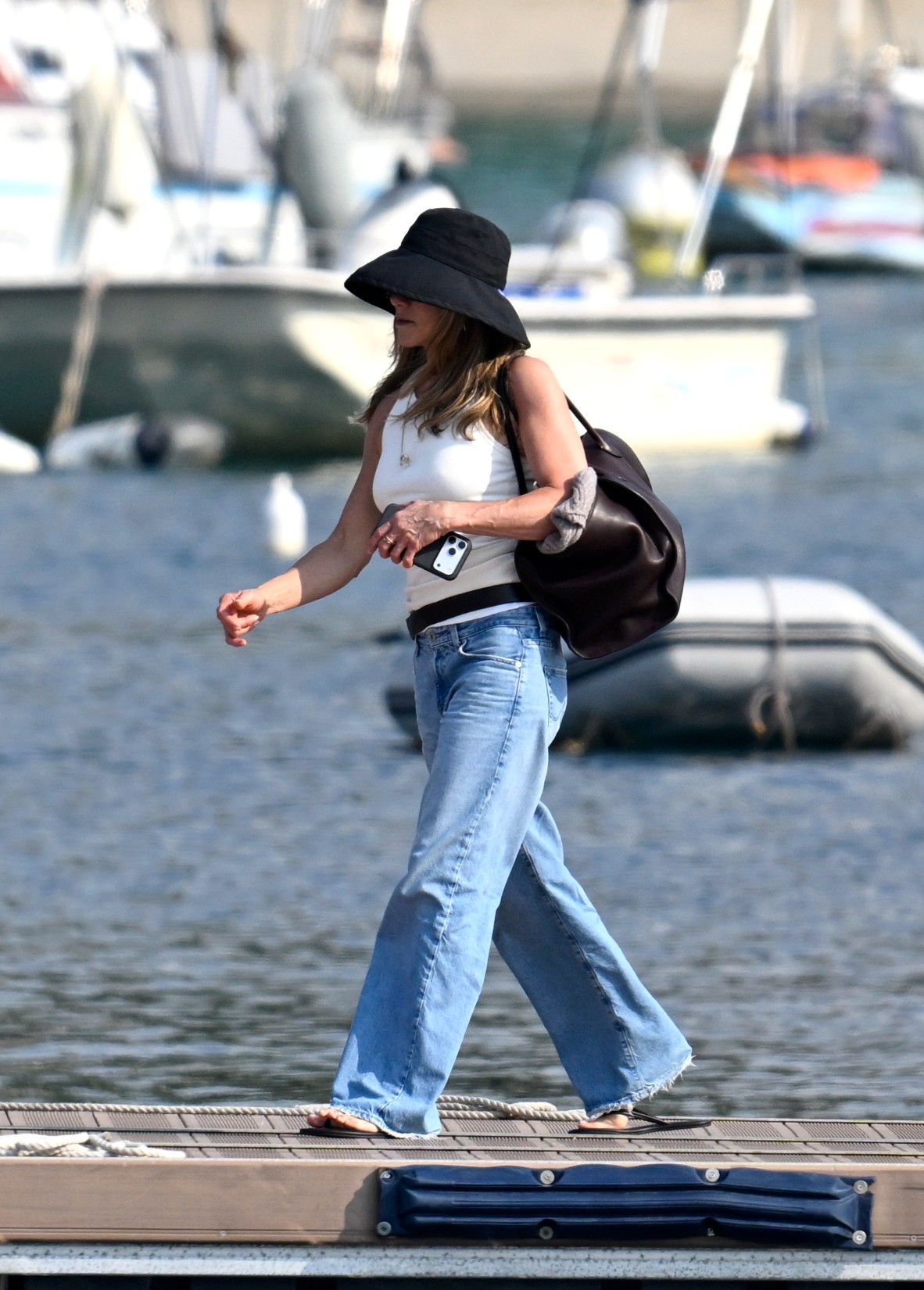 An image of Jennifer Aniston in Mallorca wearing a white tank top with bootcut jeans and black flip-flops.