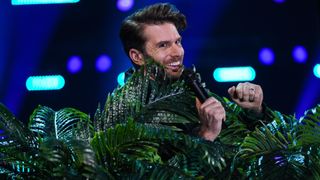 The Masked Singer I'm A Celebrity Special host Joel Dommett surrounded by fake plants