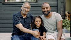 A smiling grandfather sits on a deck with his son and granddaughter.