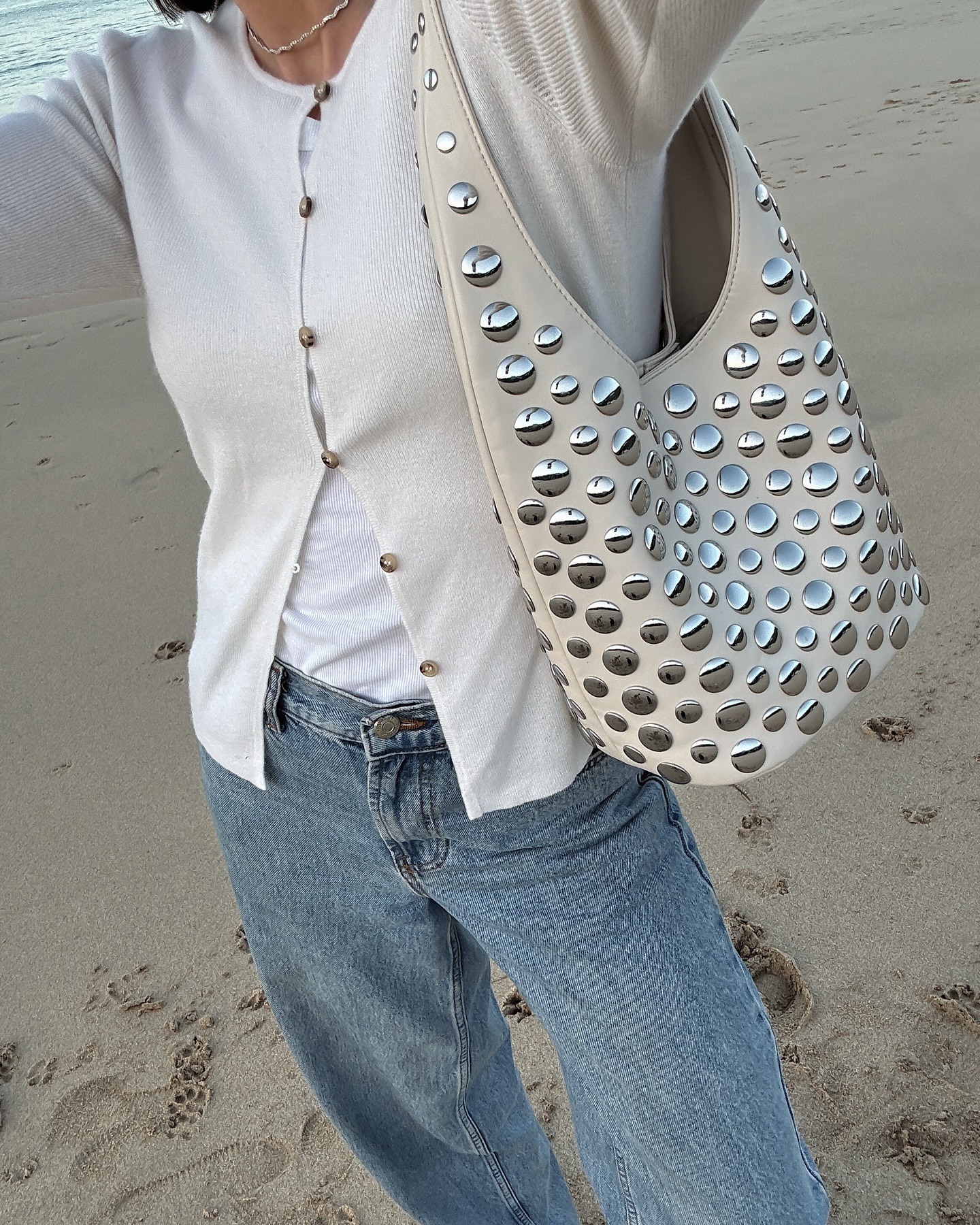 Jessica wears cream cardigan, blue jeans and studded bag