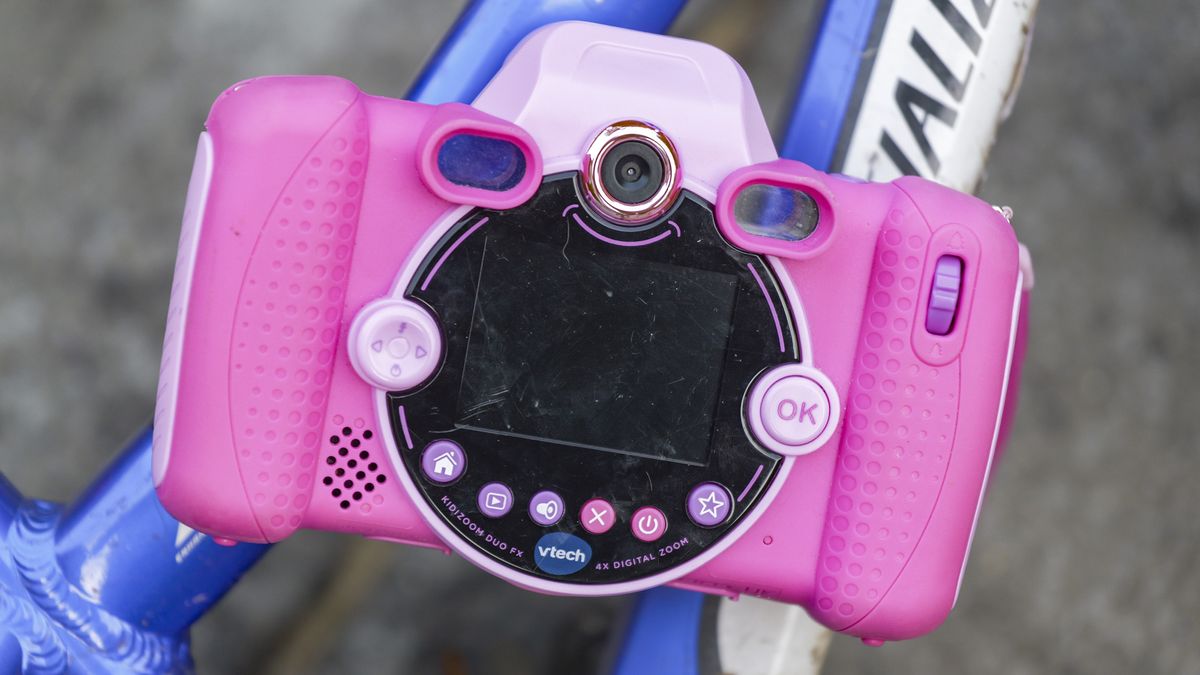 A pink V-Tech KidiZoom Duo camera resting on the blue and white frame of a kid's bike