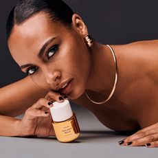  model wearing gold jewelry holding up bottle of phlur golden rule perfume