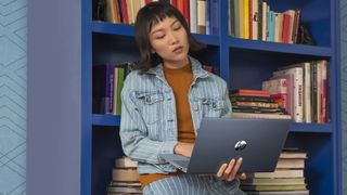 Woman leaning against a bookcase while using a laptop