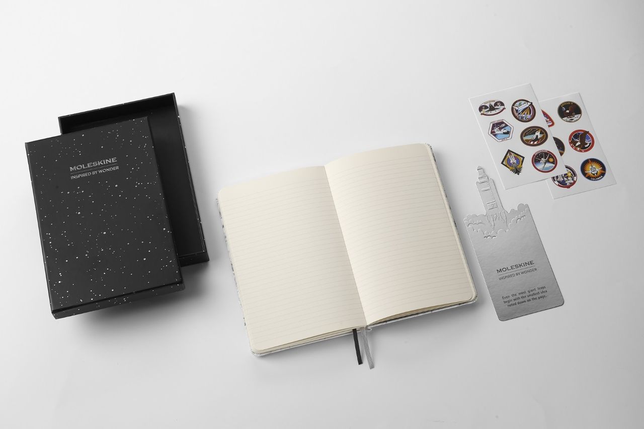 NASA-inspired Limited Edition Notebook from Moleskine gift bundle. This includes: black gift box decorated with white stars, lined notebook, bookmark of rocket blasting off with an inspirational quote ("Even the most giant leaps begin with the smallest idea noted down on the page."), and 12 NASA/space-themed stickers.