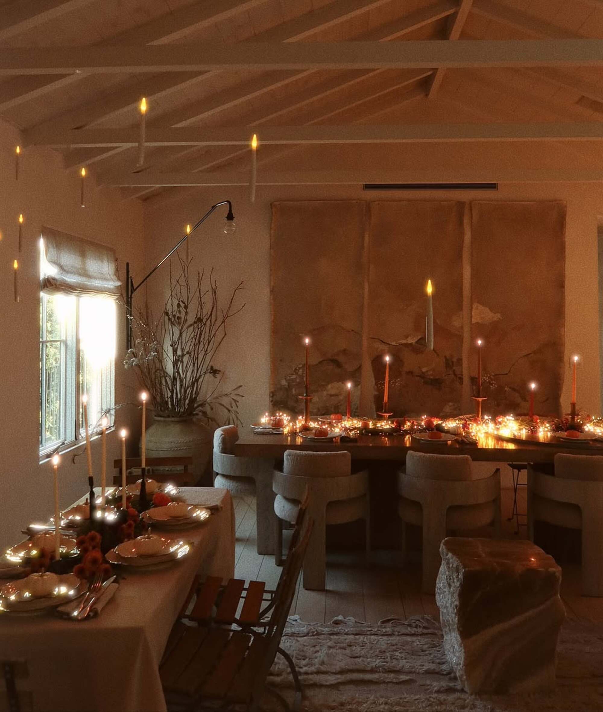 A low lit dining room with contemporary furniture and candles on two long rectangular tables