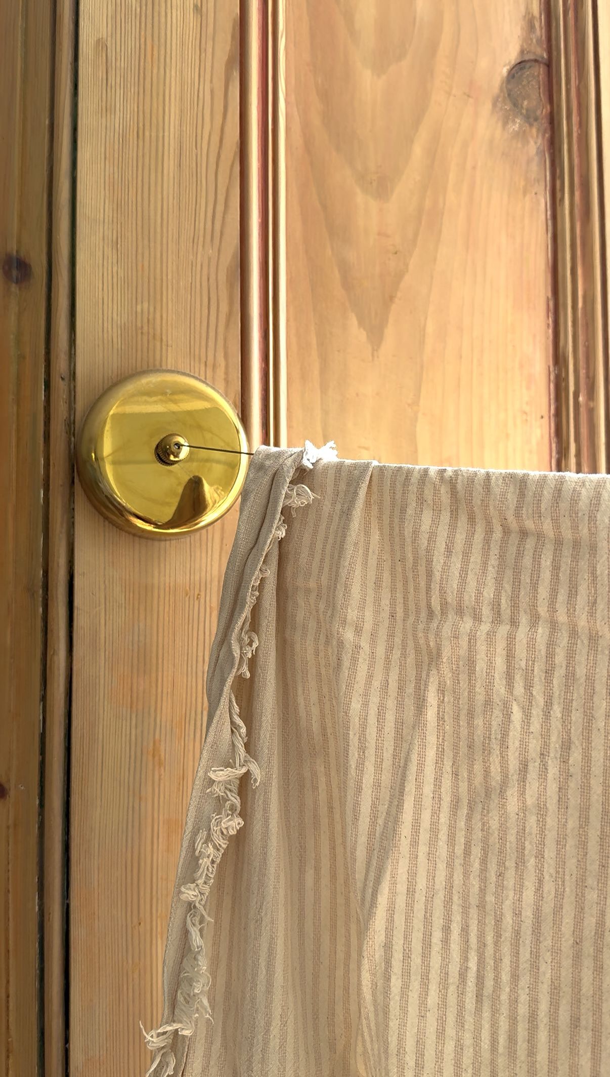 Close-up image of a brass retractable clothes line on a wooden wall. There is a beige pinstripe linen blanket on the clothesline.