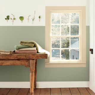 green and cream two tone wall with large window wooden table and wood floorboards