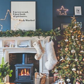 A blue-painted living room with a white fireplace decorated for Christmas with festive lights and a Christmas tree next to it