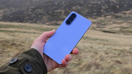 The Samsung Galaxy A57 being held over a field, showing its back.