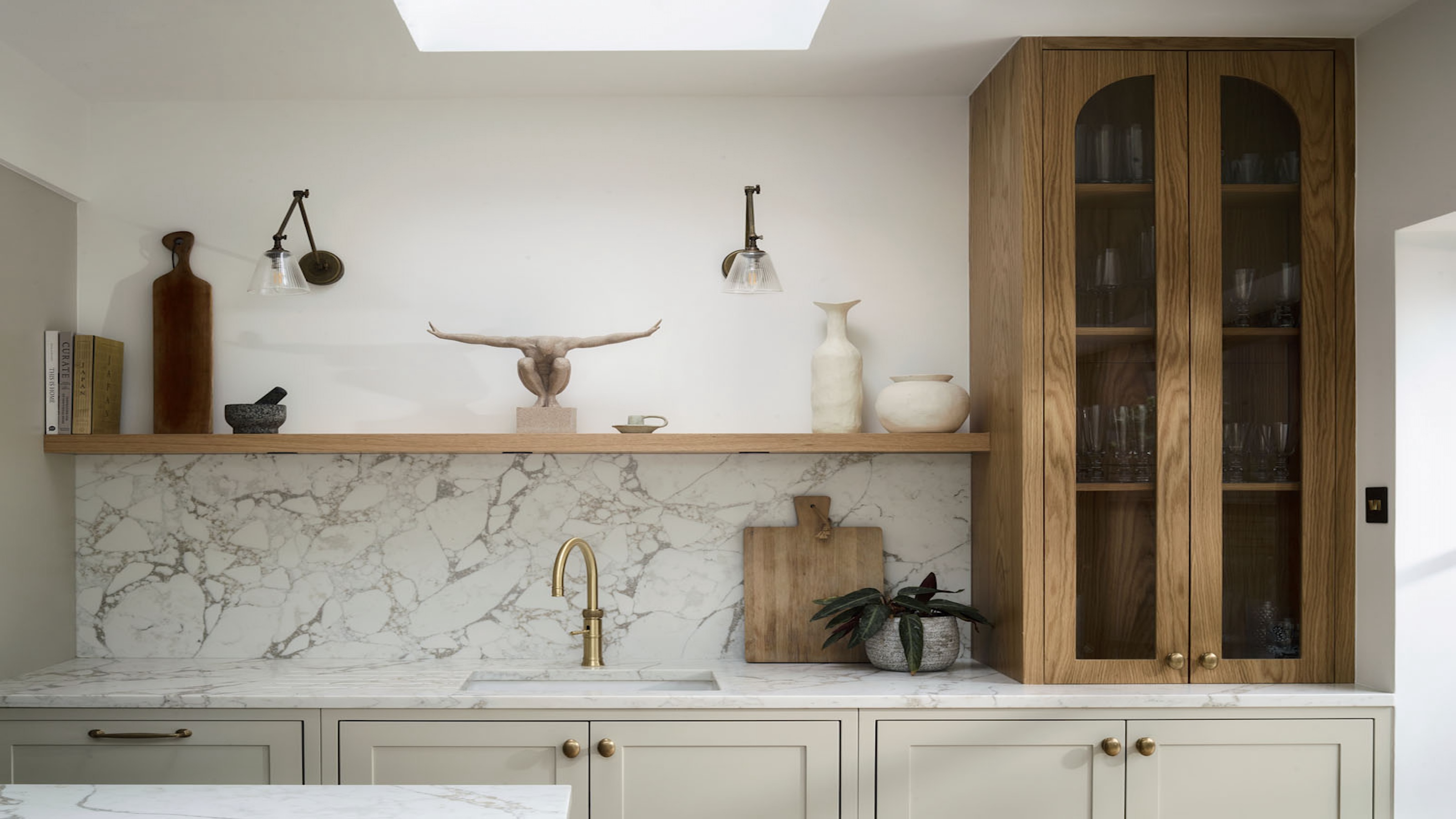 a cream shaker kitchen with an oak cupboard, marble worktops and a gold kitchen tap 