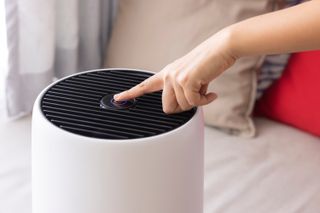 A woman pressing the on button on a white air purifier
