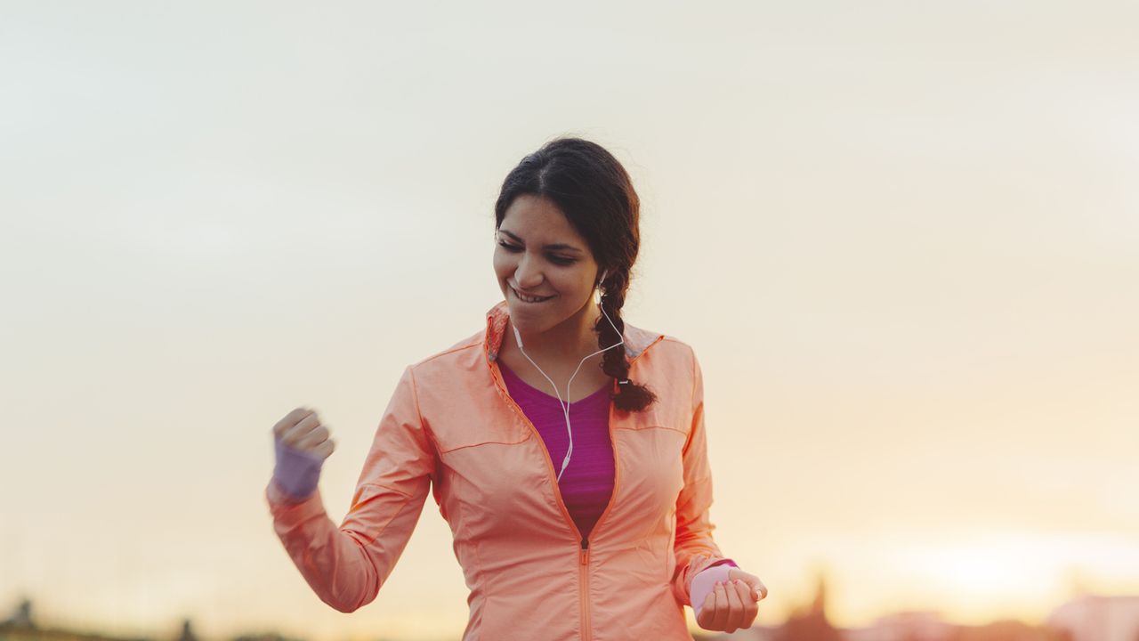 Female Runner Jogging in the city and finishing her training with her hand up in the air screaming with happiness. She made her goal!