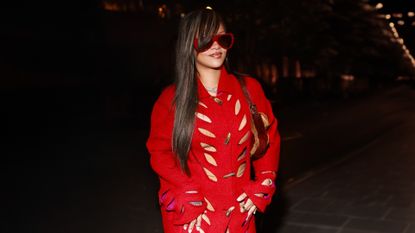 Rihanna wearing a red cutout coat from Dior, white Loewe heels, and red sunglasses.