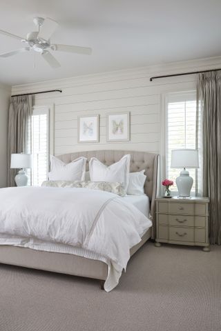 A neutral bedroom with a double bed with white bedding, wall paneling and a light graycarpet