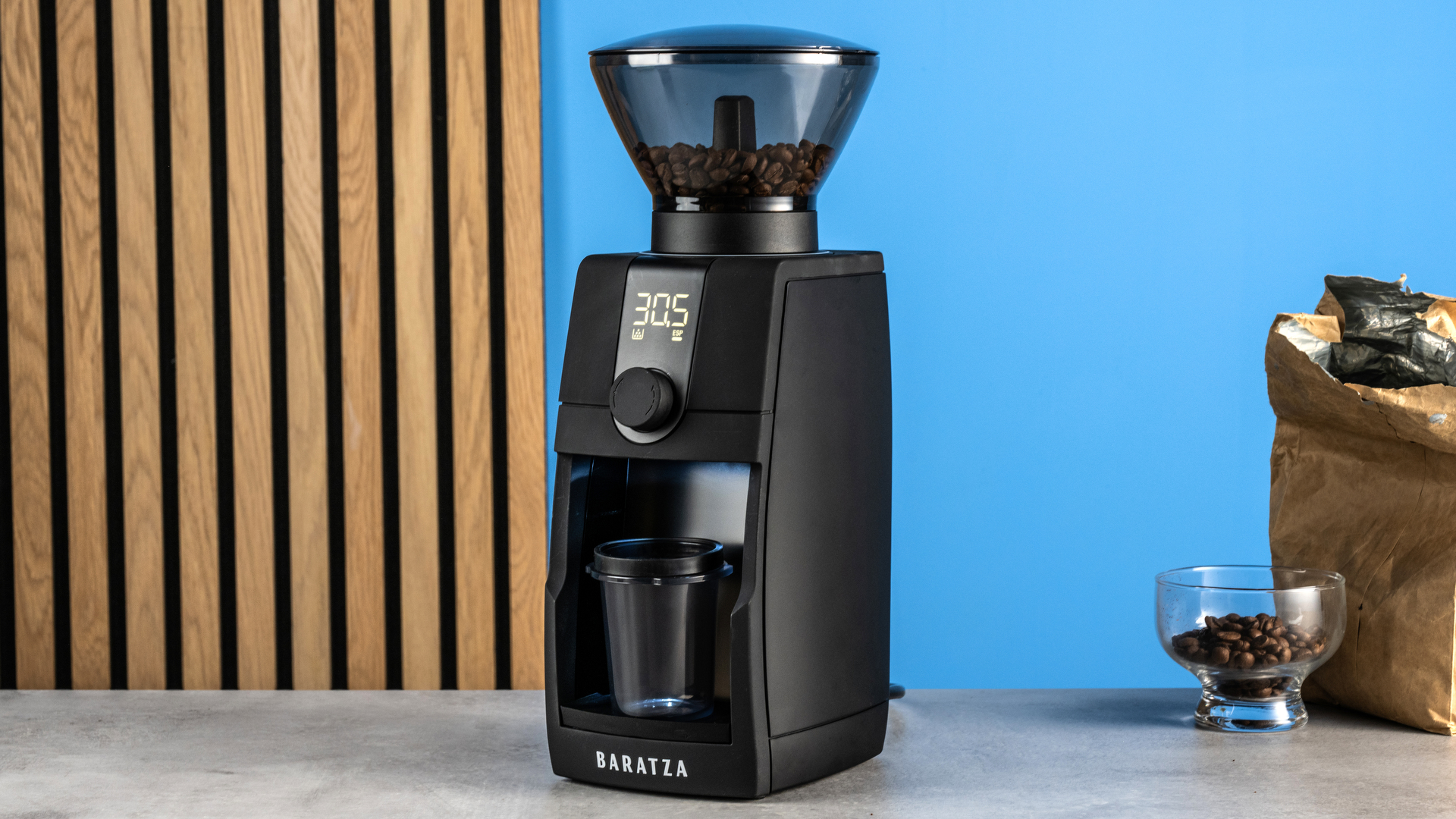 the baratza encore esp pro coffee grinder photographed against a blue tom's guide background with a bag of coffee to the side and showing the grinder in action