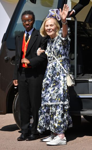 The Duchess of Kent wearing a purple and white floral dress with white sneakers waving while holding the arm of a staff member at Prince Harry and Meghan Markle's wedding