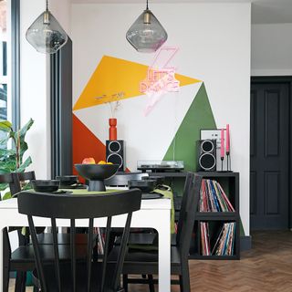 a dining table and chairs with bold colourful paint effect on the wall and a neon sign