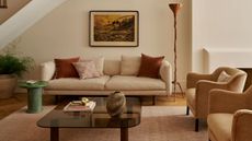 A warm living room with a white couch and colorful pillows, a textured orange-brown floor lamp, a green stone side table, a potted plant, a low glass coffee table, a large rug, and a pair of chairs